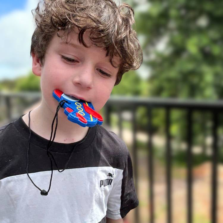 Child wearing a colorful mouthguard outdoors with greenery in the background