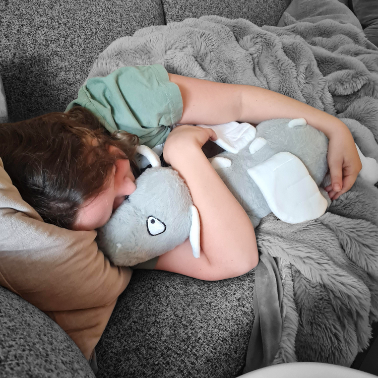 Child hugging a large gray elephant plush toy on a couch