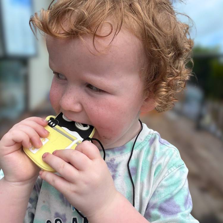 Child holding a yellow toy with a blurred outdoor background
