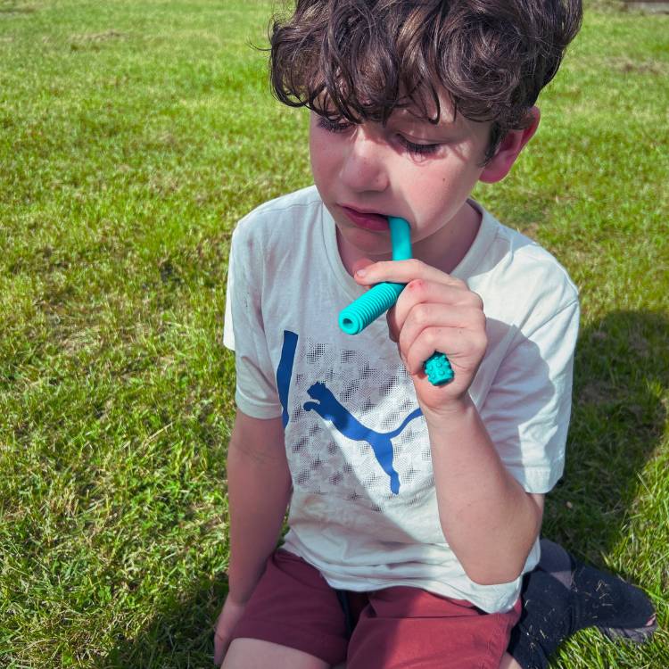 Child sitting on grass holding a blue object, wearing a white Puma shirt