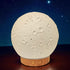 Moon-shaped lamp with wooden base against a starry night sky