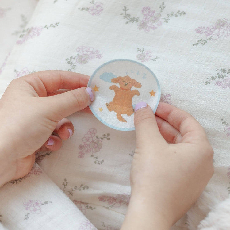 Hand holding a round sticker with a cartoon dog on a floral fabric background