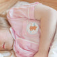 Person wearing a pink outfit with a cartoon character patch, lying on a wooden floor.