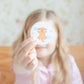 Person holding a round sticker with a cartoon dog design against a blurred background