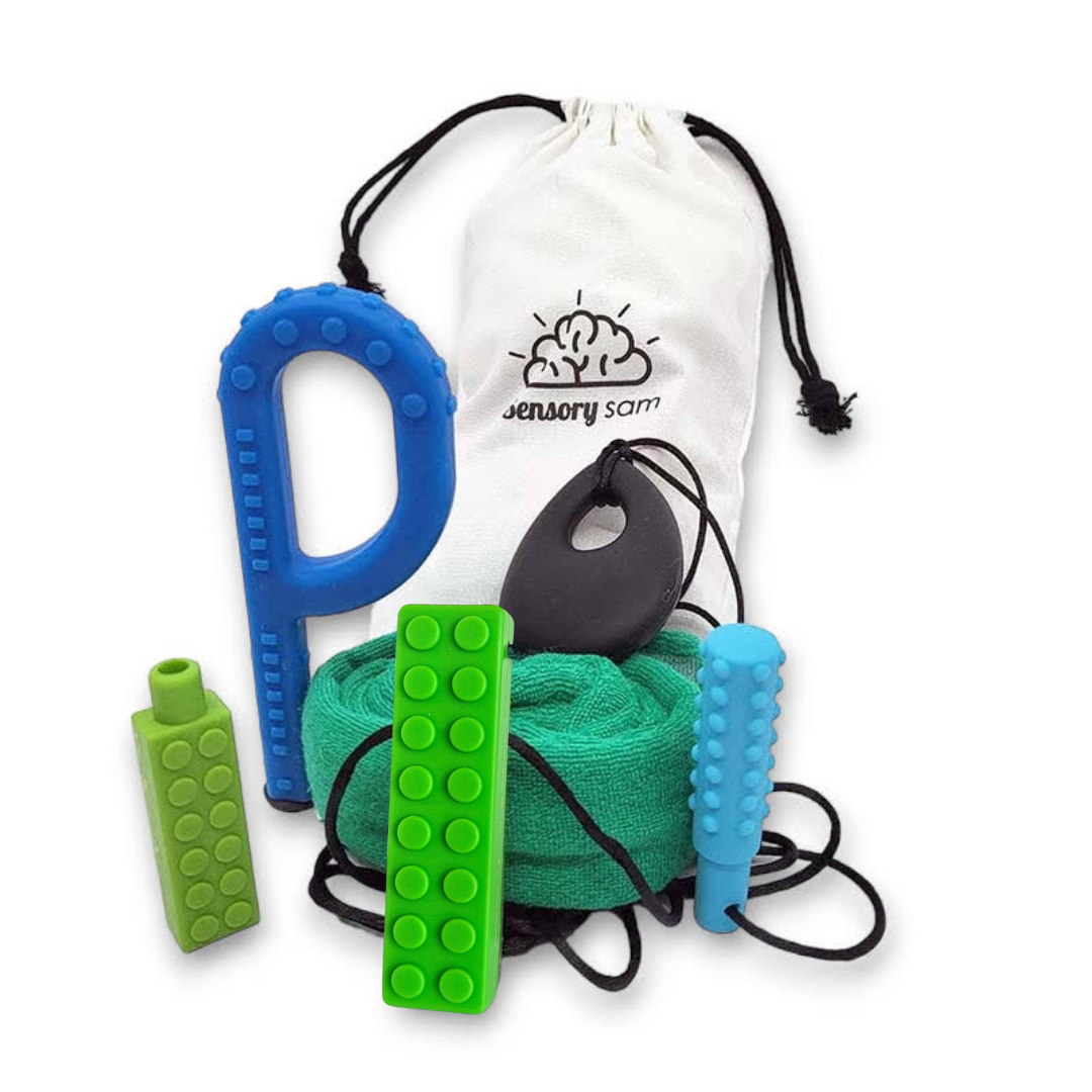A collection of chewable toys and accessories including a blue chew stick, green block chewies, a black pendant, and a blue chewable band, presented alongside a white canvas bag with the product name &