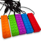 A selection of chew necklaces in various colors including orange, green, purple, blue, and red, with a textured block design.