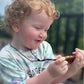 Young child outdoors holding a brown pendant on a black cord.