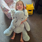 Child holding a large stuffed elephant toy on a carpeted floor with toys in the background.