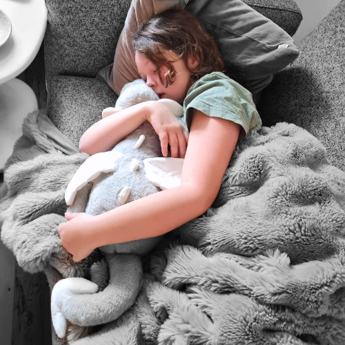 A child appears to be sleeping soundly, hugging a gray weighted dragon toy tightly.