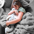 A child appears to be sleeping soundly, hugging a gray weighted dragon toy tightly.
