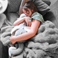 A child appears to be sleeping soundly, hugging a gray weighted dragon toy tightly.