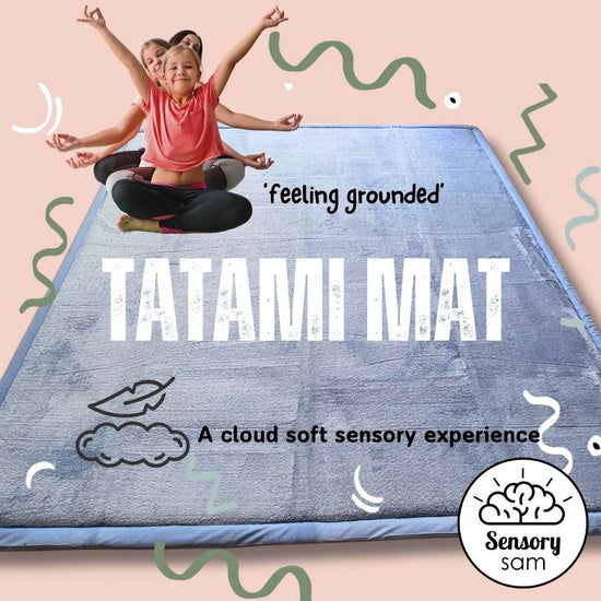 A child sitting cross-legged on a grey/tan memory foam tatami mat with raised hands, with decorative elements around the mat.