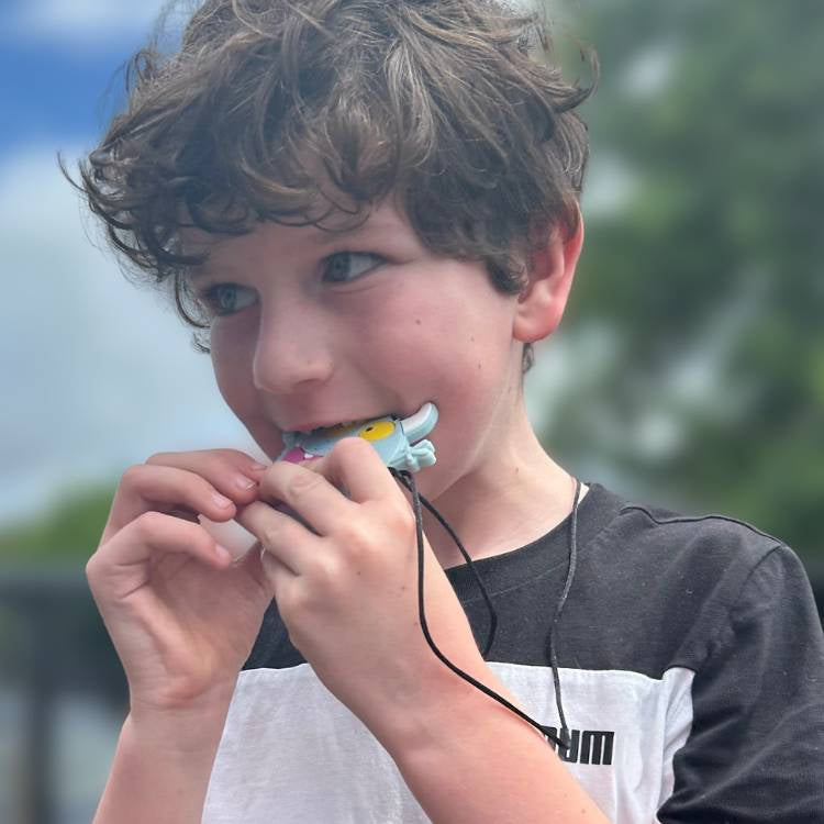 Child holding a small toy or device close to their mouth with a blurred outdoor background