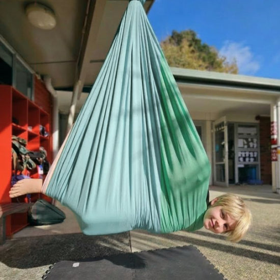 Person in a green hammock outside a building with red shelves.