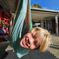Child hanging upside down in a green fabric swing with a school building in the background
