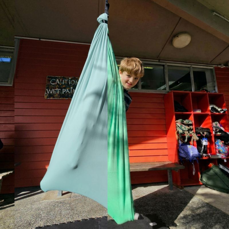 Child in a green hammock hanging from the ceiling in an outdoor setting.