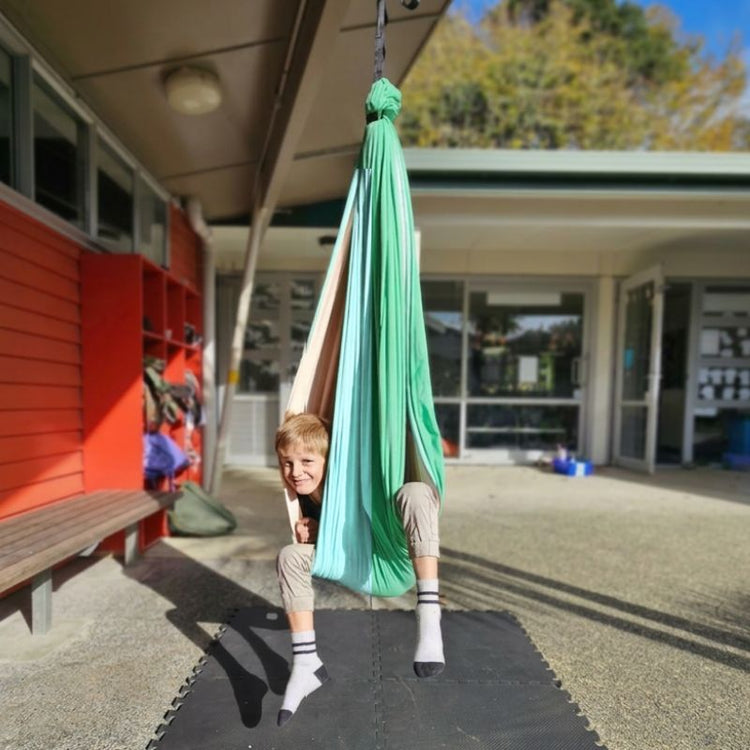 Child in a green swing outside a building with red lockers.