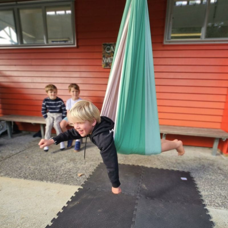 Child in a green swing set with two other children in the background.