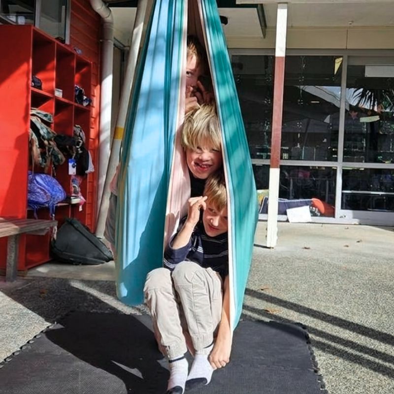 Children playing inside a blue fabric tent on a school playground.