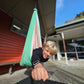 Person hanging from a green and pink hammock outside a building with a clear sky.