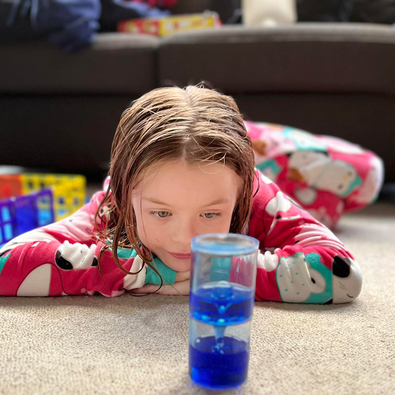 A child lying on the floor looking at a sensory liquid cylinder toy with thick pink gloopy jelly.