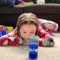A child lying on the floor looking at a sensory liquid cylinder toy with thick pink gloopy jelly.