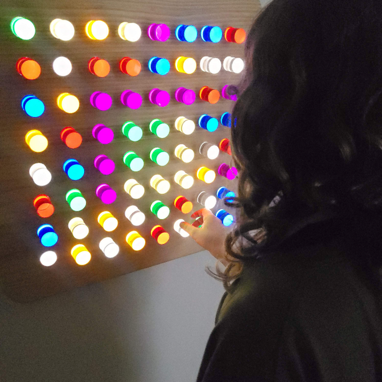 A person interacting with a multicolored LED acrylic light wall, with lights in various colors illuminated in a pattern.