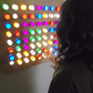 A person interacting with a multicolored LED acrylic light wall, with lights in various colors illuminated in a pattern.