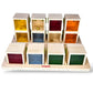 Colorful wooden cube puzzle with transparent sides, each containing small objects, on a white background. Brand &