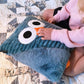 Child playing with a blue pillow shaped like an owl on a patterned floor.