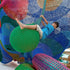 A child playing on a colorful, crochet-textured swing designed to resemble a wrecking ball, hanging from a ceiling.