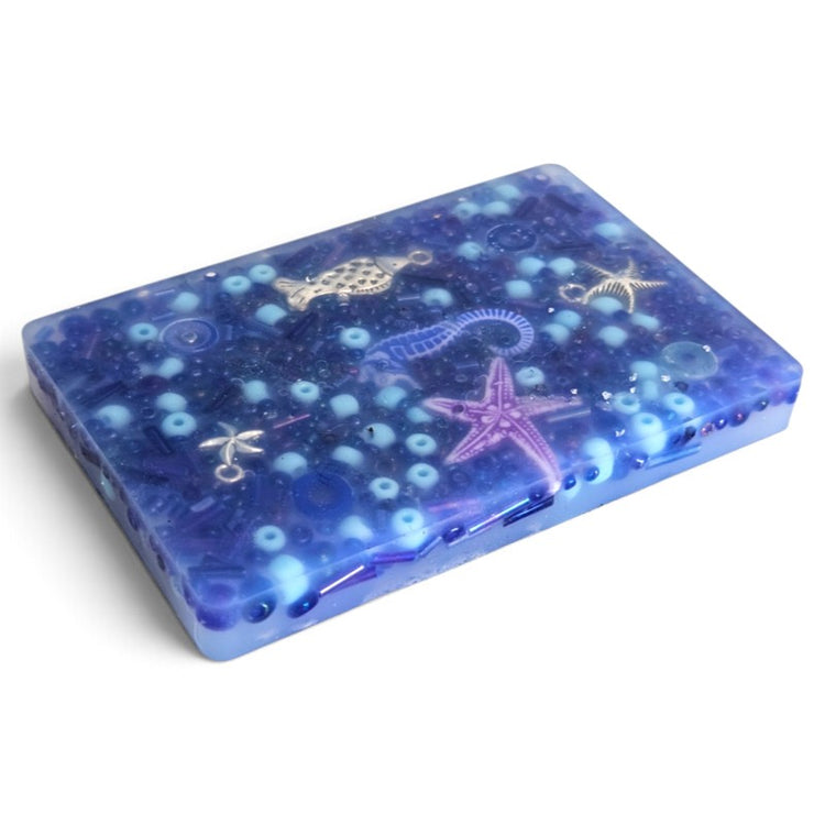 Blue rectangular resin sensory tray with beads, a purple starfish and other ocean-themed shapes.