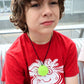 Child wearing a red shirt with a graphic design and a green necklace, sitting on a couch.