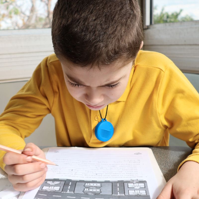 Child in yellow shirt with blue device on neck, writing on paper