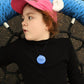 Child wearing a pink helmet with a blue tag, sitting in a stroller.