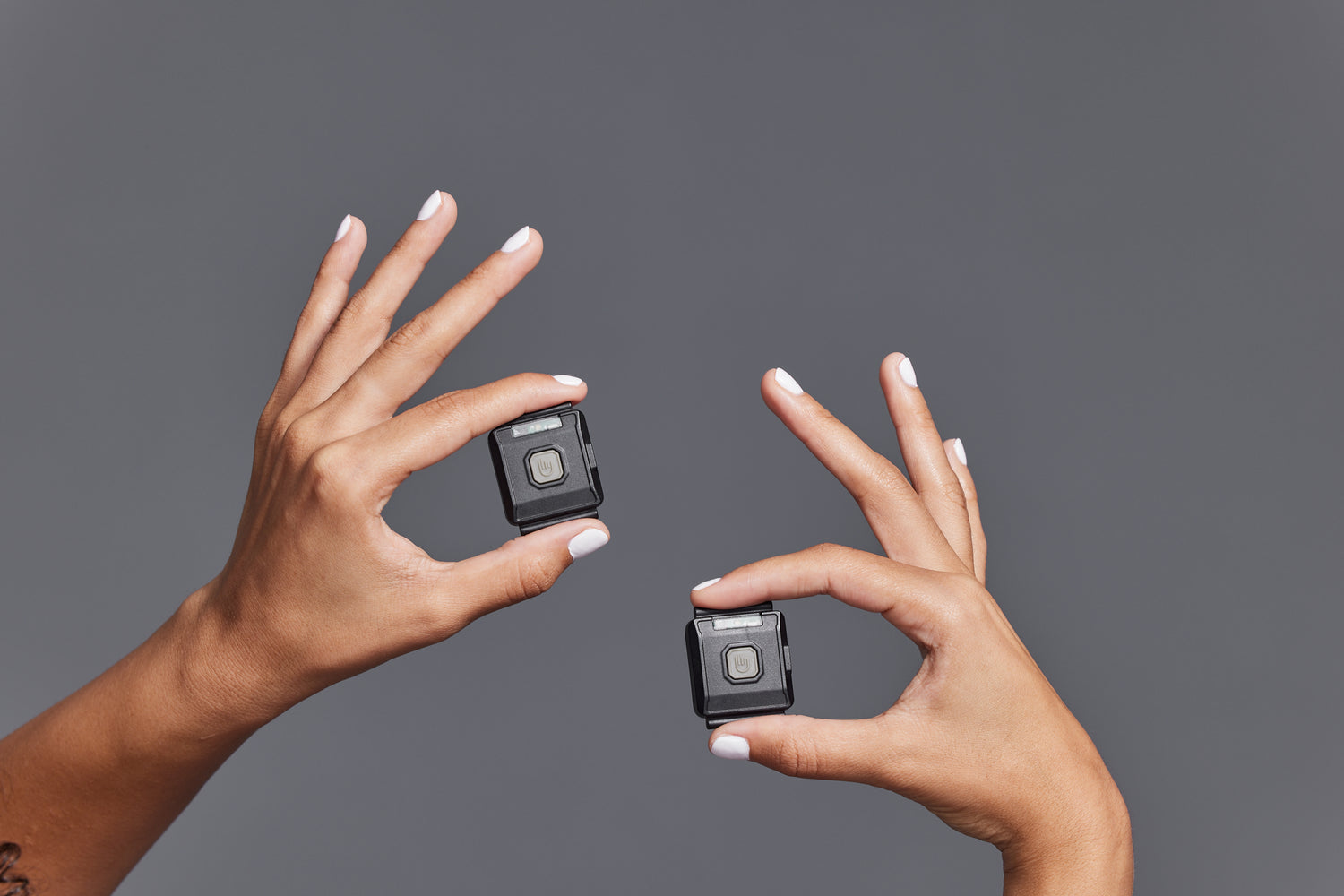 Two hands holding small black square devices against a gray background