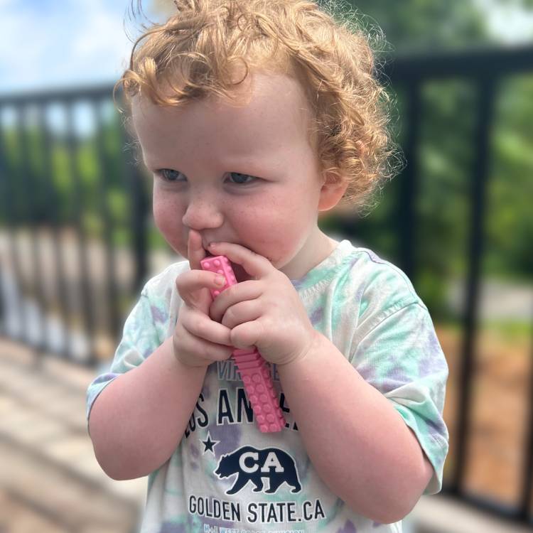 Child holding a pink object outdoors on a wooden deck