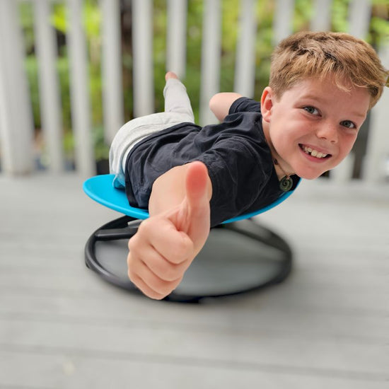 A child giving a thumbs up while sitting on a blue spinning seat designed to provide sensory input.