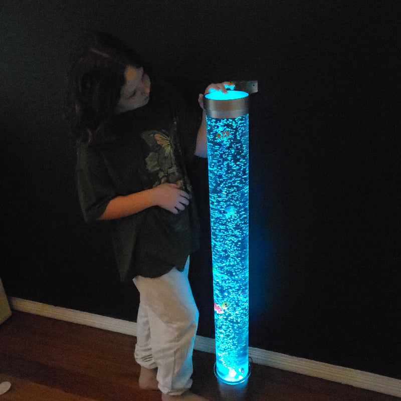 A person standing next to a tall cylindrical LED bubble tube lamp that is lit up with blue bubbles visible inside it.