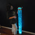 A person standing next to a tall cylindrical LED bubble tube lamp that is lit up with blue bubbles visible inside it.