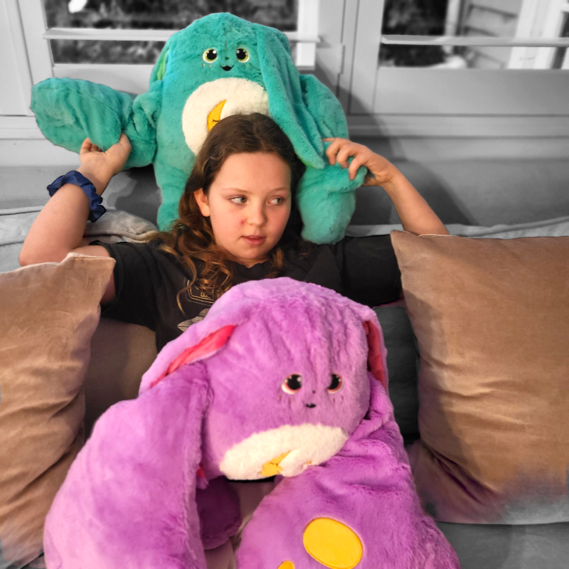 Child seated with green and purple weighted monster plush toys