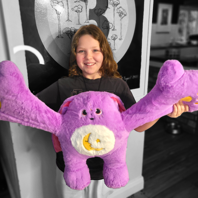 Child holding a large purple weighted monster plush toy with arms spread out