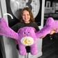 Child holding a large purple weighted monster plush toy with arms spread out