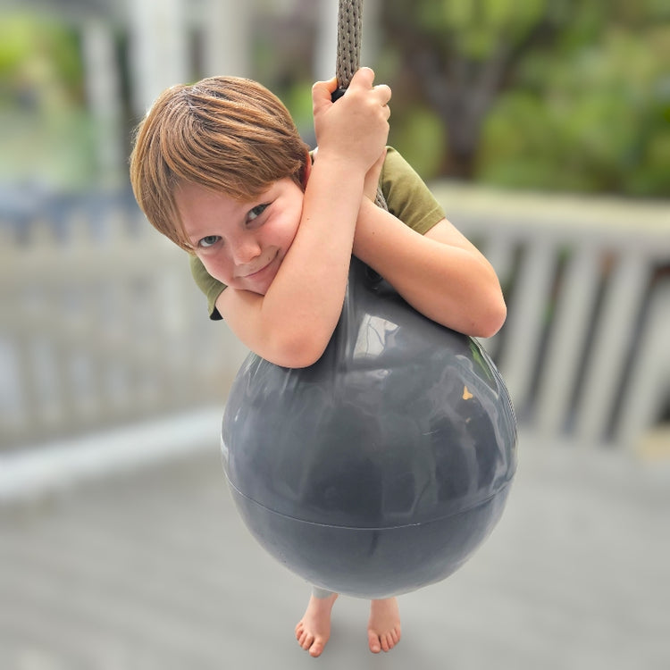 Child playing on a large gray ball swing outdoors