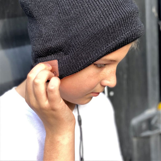 A person wearing a gray knit beanie with built-in wireless headphones, listening to music.