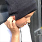 A person wearing a gray knit beanie with built-in wireless headphones, listening to music.