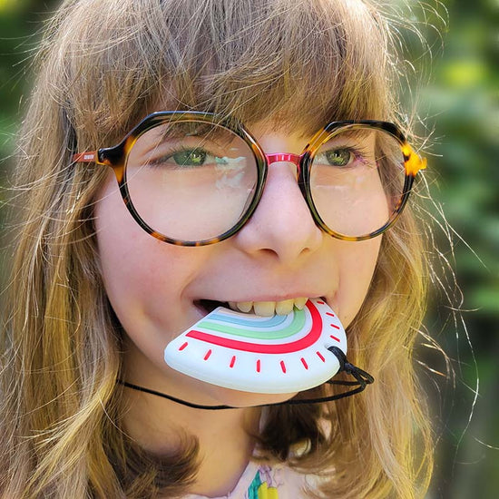 A child with glasses is wearing a chewie necklace with a large rainbow pendant.