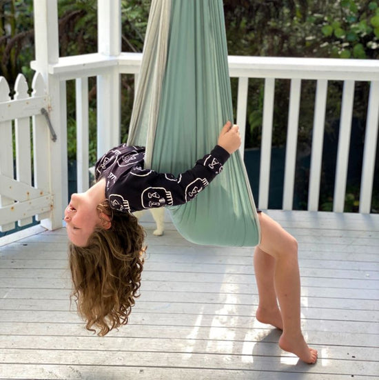A child enjoying a sensory swing made of double layered cotton spandex in a duck egg blue color, hanging outdoors.