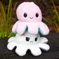 A plush toy resembling an octopus with reversible facial expressions, one side happy and one side sad, set against a natural background.