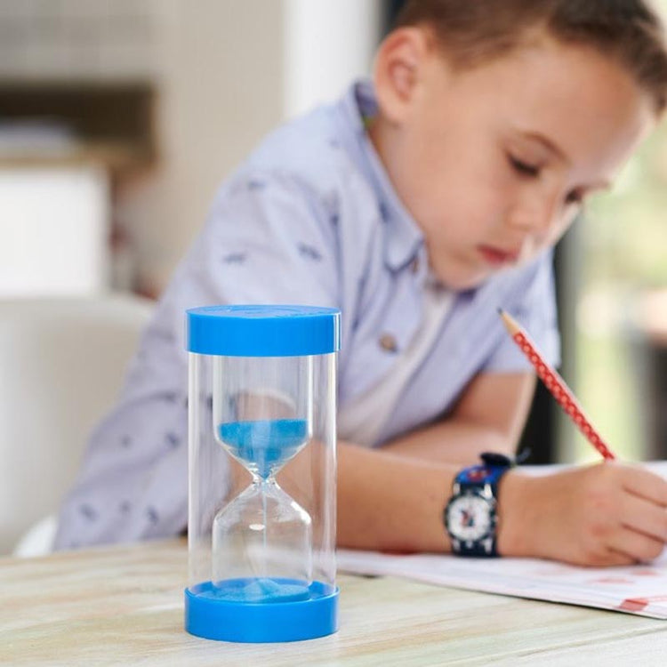 A child sitting at a table with a blue and clear sand timer.
